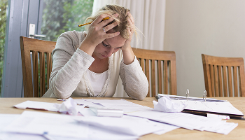 Woman sitting at a table looking stressed while looking at a pile of bills and papers