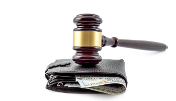 Wooden gavel resting on a black leather wallet containing a stack of hundred-dollar bills